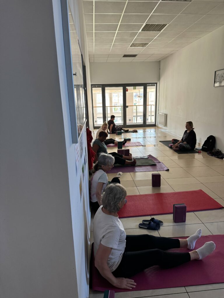 Osoby siedzące na korytarzu na matach do pilatesu