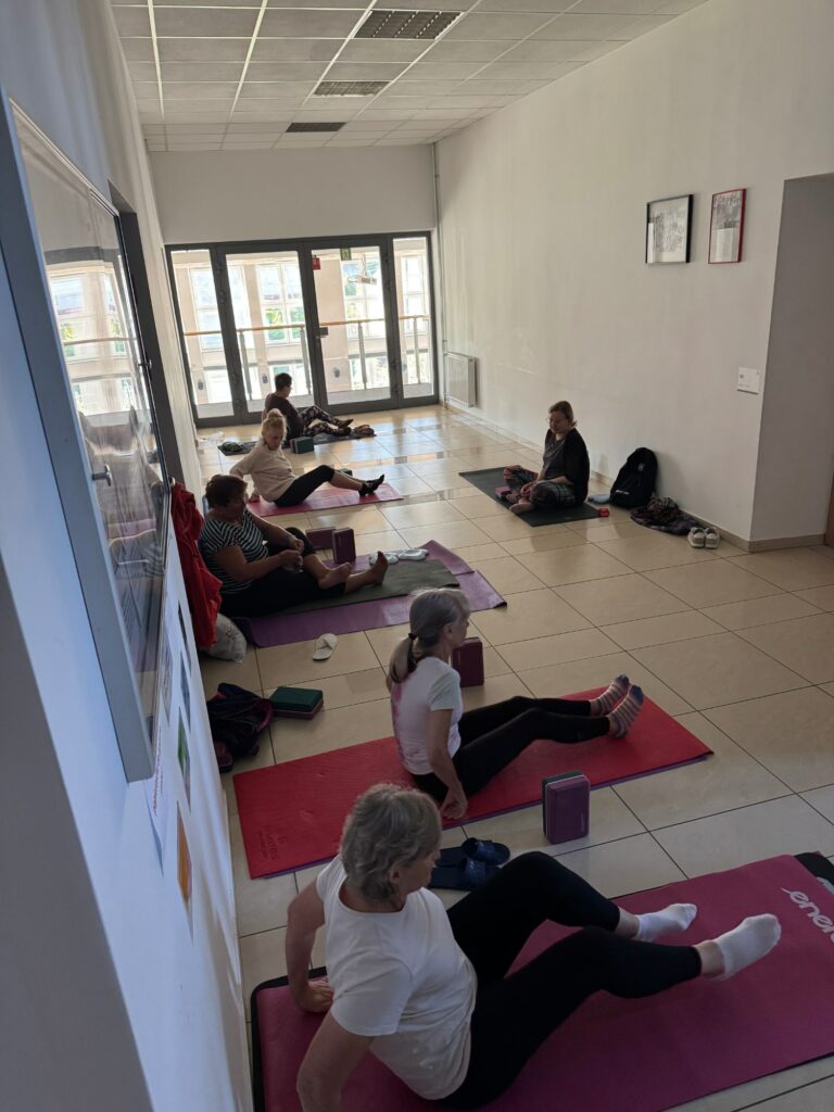 Osoby siedzące na korytarzu na matach do pilatesu