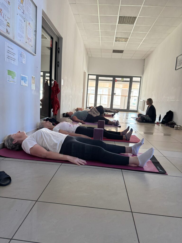 Osoby siedzące na korytarzu na matach do pilatesu